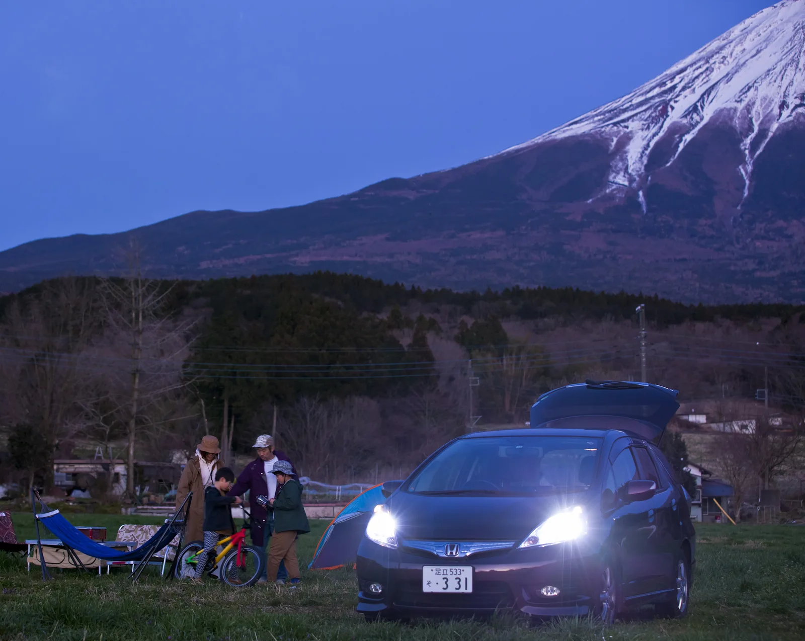 日暮れの富士山のふもとで、LEDヘッドライトを点灯した車